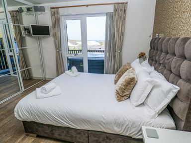A bedroom with a bed with pillows and rolled towels near a window with curtains and a wall-mounted TV at Bay View Portreath