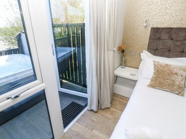 A bedroom with a bed a bedside table with a glass vase and a flower and a door leading to a balcony with a hot tub at Bay View in Portreath