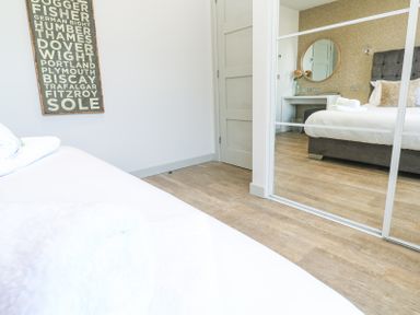 A bedroom with a bed and a mirror door wardrobe reflecting a vanity table with a round mirror and a bed at Bay View in Portreath