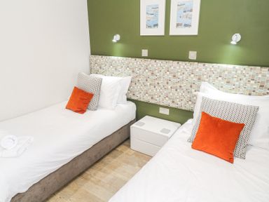 A bedroom with two single beds orange and patterned pillows and a white nightstand between the beds at Bay View in Portreath