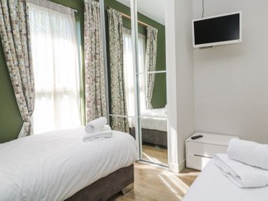 A bedroom with two beds white bedding a wall-mounted TV and mirrored wardrobe at Bay View in Portreath
