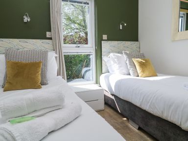 A bedroom with two single beds with patterned headboards and cushions by a window at Bay View in Portreath