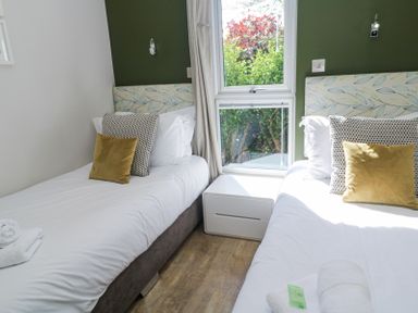 A bedroom with two single beds with patterned headboards and cushions separated by a window and a white bedside table at Bay View in Portreath