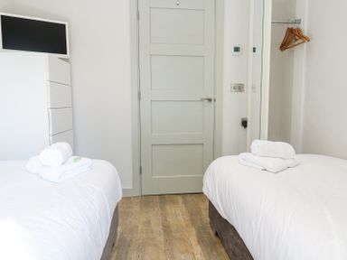 A bedroom with two beds a TV on a chest of drawers a door and a wall mirror at Bay View in Portreath
