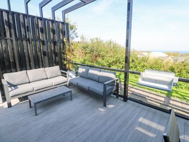 An outdoor patio with two grey sofas a metal coffee table potted plants and a barbecue grill at Bay View in Portreath