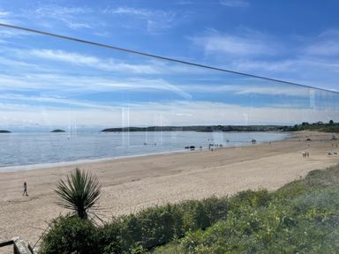 A sandy beach with people walking and boats on the water with a grassy area in the foreground at The Warren M45 in Abersoch