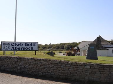 An outdoor scene with a stone wall a sign for Clwb Golff Abersoch a building and a large stone monument at The Warren M45 in Abersoch