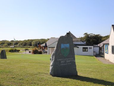 A stone monument with an inscription on a grassy area near white buildings at The Warren M45 in Abersoch
