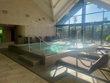 An indoor pool with water jets surrounded by lounge chairs and large windows letting in daylight at The Warren M45 in Abersoch