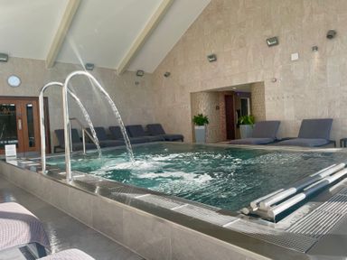 An indoor pool with water features surrounded by lounge chairs at The Warren M45 in Abersoch