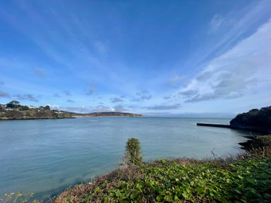 A view of a bay with water and rocky shoreline with houses on the left and a pier on the right at The Warren M45 in Abersoch