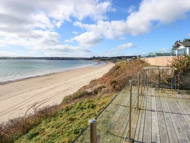 A wooden deck with glass railing and bar stools overlooking a sandy beach and sea at The Warren M45 in Abersoch