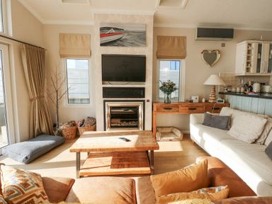 A living room with a television above a fireplace and a wooden coffee table at The Warren M45 in Abersoch