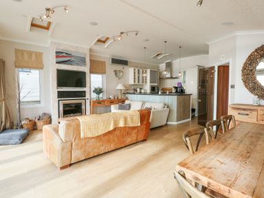 An open plan living room kitchen and dining area with a leather sofa a wooden dining table and chairs and a kitchen island at The Warren M45 in Abersoch