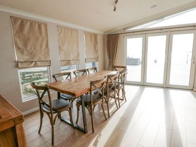 A dining area with a wooden table and six chairs near windows and glass doors at The Warren M45 in Abersoch