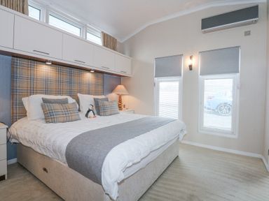 A bedroom with a large bed with pillows and a stuffed penguin under cabinets and windows at The Warren M45 in Abersoch