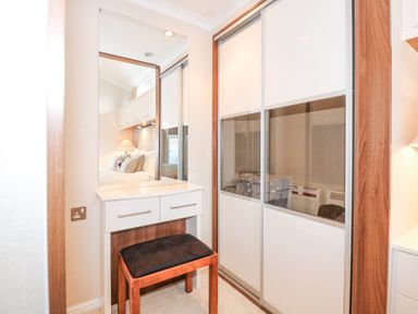 A dressing area with a mirror desk and stool next to a wardrobe with sliding doors at The Warren M45 in Abersoch