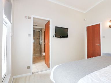 A bedroom with a bed a wall-mounted television an open door to a bathroom and a closed door at The Warren M45 in Abersoch