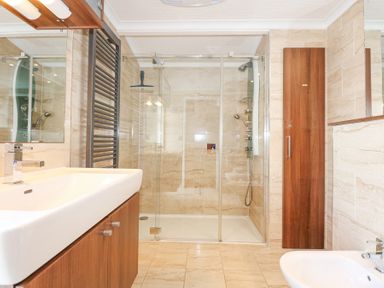 A bathroom with a shower enclosure a sink with wooden cabinet a bidet and a wooden storage unit at The Warren M45 in Abersoch