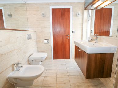 A bathroom with a wooden door a wall-mounted toilet a bidet a sink with cabinet and two mirrors at The Warren M45 in Abersoch