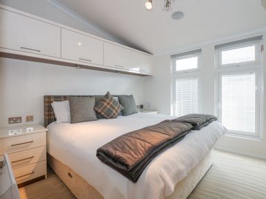 A bedroom with a large bed, cushions, overhead cabinets, bedside drawers, and windows with blinds at The Warren M45 in Abersoch