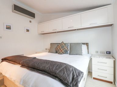 A bedroom with a double bed pillows and a blanket under wall cabinets at The Warren M45 in Abersoch