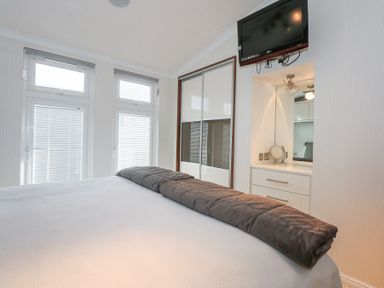A bedroom with a bed a blanket on it windows with blinds a wardrobe and a wall mounted tv at The Warren M45 in Abersoch