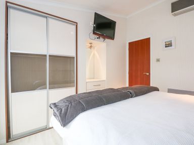 A bedroom with a bed a blanket a wardrobe a mounted television a wooden door and a dresser with a mirror at The Warren M45 in Abersoch