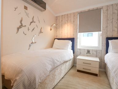 A bedroom with two single beds a window between them and a nightstand at The Warren M45 in Abersoch