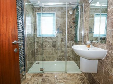 A bathroom with a glass shower enclosure a sink a wooden door and a window at The Warren M45 in Abersoch