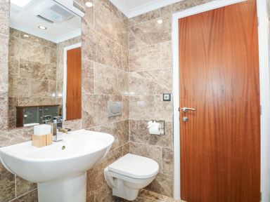 A bathroom with a wall-mounted toilet and a pedestal sink with a mirror above at The Warren M45 in Abersoch