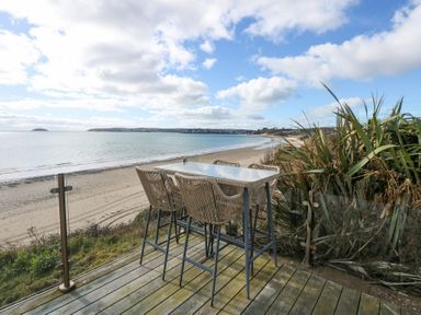 An outdoor deck with a table and four chairs overlooking a sandy beach and ocean at The Warren M45 in Abersoch