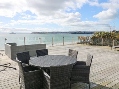 An outdoor deck with a round table and six chairs overlooking the sea at The Warren M45 in Abersoch