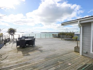 A large wooden deck with outdoor chairs and tables overlooking the sea with distant islands at The Warren M45 in Abersoch