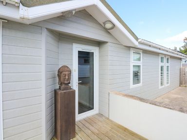 An exterior deck area with a Buddha head statue on a pedestal next to a glass door and grey siding on the building at The Warren M45 in Abersoch
