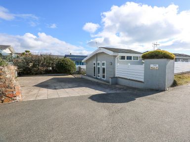 A small detached house with a tiled roof and multiple windows surrounded by a paved driveway and bushes at The Warren M45 in Abersoch