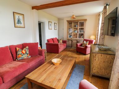 A living room with red sofas wooden furniture and framed pictures at Ivy Cottage in Colerne