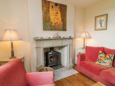 A living room with a wood burning stove fireplace two red sofas lamps and paintings at Ivy Cottage in Colerne
