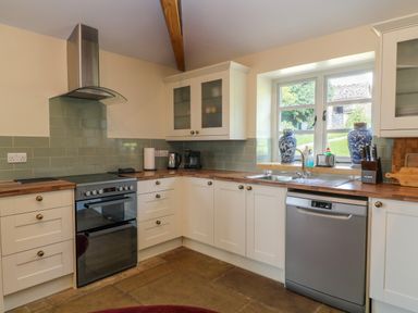 A kitchen with white cabinets wood countertops a stove dishwasher window with blue and white vases and a stainless steel sink at Ivy Cottage in Colerne