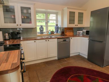 A kitchen with white cabinets wooden countertops a stainless steel refrigerator dishwasher and oven with a window above the sink at Ivy Cottage in Colerne