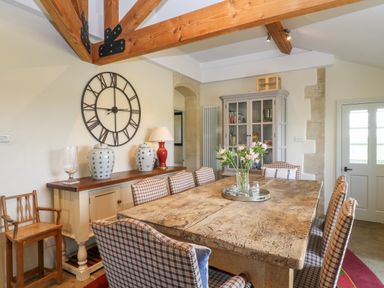 A dining room with a wooden table surrounded by plaid upholstered chairs and a sideboard with decorative items at Ivy Cottage in Colerne