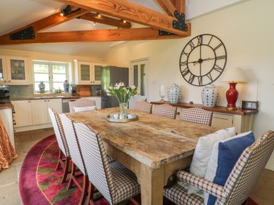 A dining area with a large wooden table surrounded by checkered chairs in an open kitchen at Ivy Cottage in Colerne