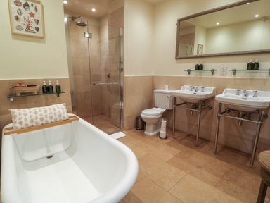A bathroom with a bathtub a glass shower two sinks a toilet and a large mirror at Ivy Cottage in Colerne
