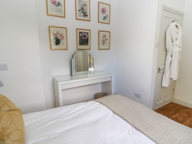 A bedroom with a white dressing table mirror six framed pictures on wall a door with robes hanging at Ivy Cottage in Colerne