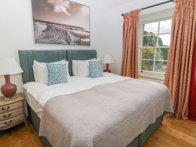 A bedroom with a large bed two bedside tables with lamps patterned curtains and a window at Ivy Cottage in Colerne