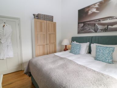 A bedroom with a bed with blue patterned pillows a wooden wardrobe a lamp and bathrobes hanging on a door at Ivy Cottage in Colerne