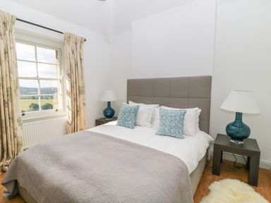 A bedroom with a double bed two side tables with lamps a window with curtains and a small rug on the floor at Ivy Cottage Colerne