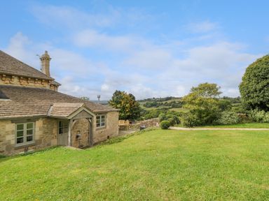 A stone house with a grassy yard and outdoor seating overlooking green hills at Ivy Cottage in Colerne
