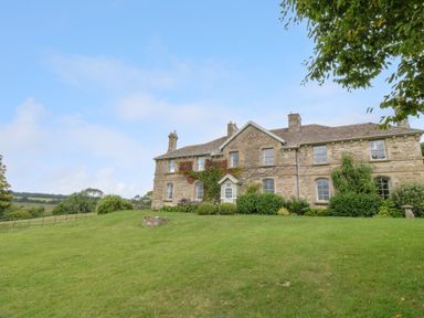 A stone house with ivy on the walls and a lawn in front at Peartree in Colerne
