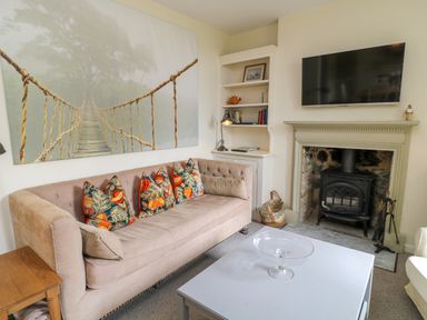 A living room with a beige sofa and patterned cushions a white coffee table a fireplace with a wood stove a mounted TV and built in shelves at Peartree in Colerne